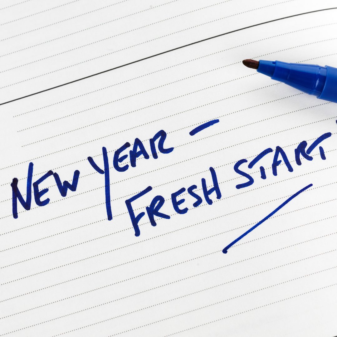 The image shows a close-up of a white lined notebook page with blue handwriting that says "NEW YEAR - FRESH START" and a blue marker pen resting on the page.