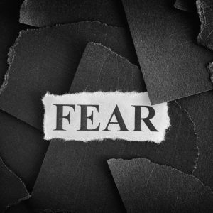 black scrap pieces of paper with a white scrap paper saying "fear" over them,