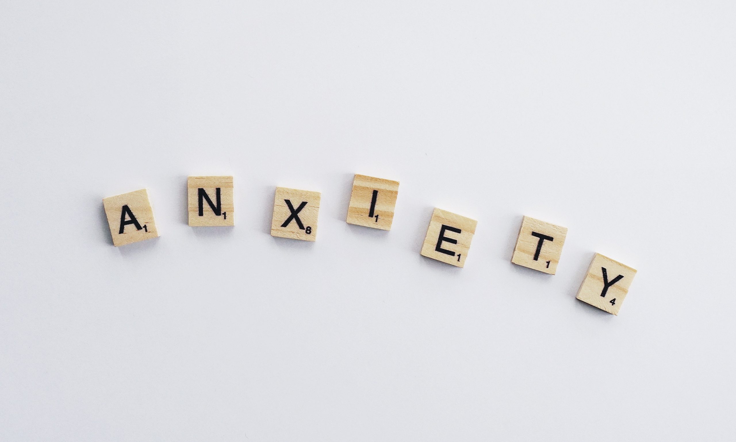 The image shows wooden tiles spelling out the word "ANXIETY" on a white background.